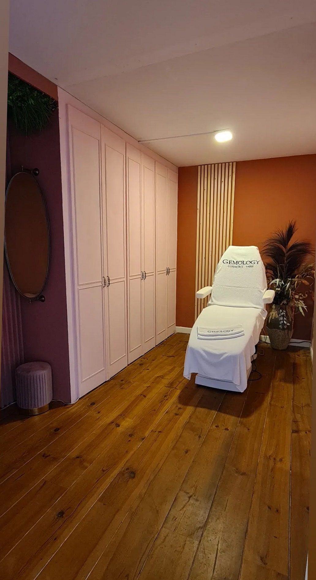 De behandelkamer met een behandelstoel voor een oranje wand en houten vloer