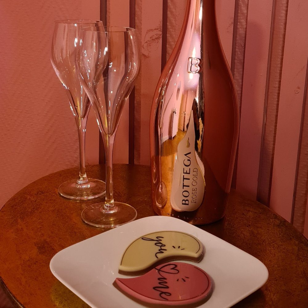 Twee glazen en een fles bubbels op een rond tafeltje voor de roze lamellenwand