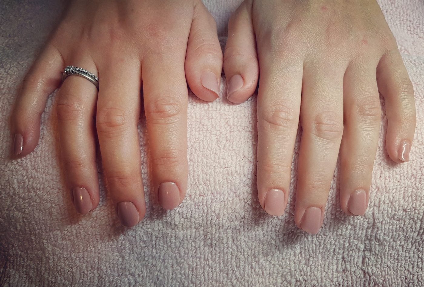 Verzorgde nagels in een zachte nudetint op een roze handdoek
